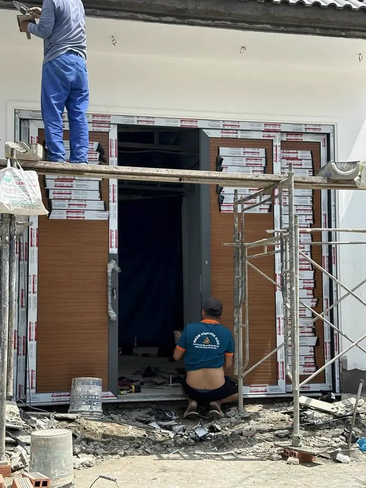 Thợ lắp cửa nhôm vân gỗ trên giàn giáo tại công trình